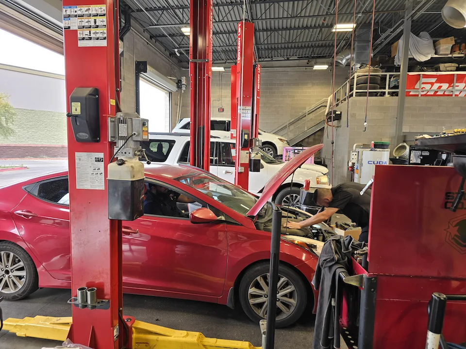 technician looking under hood of red car troubleshooting